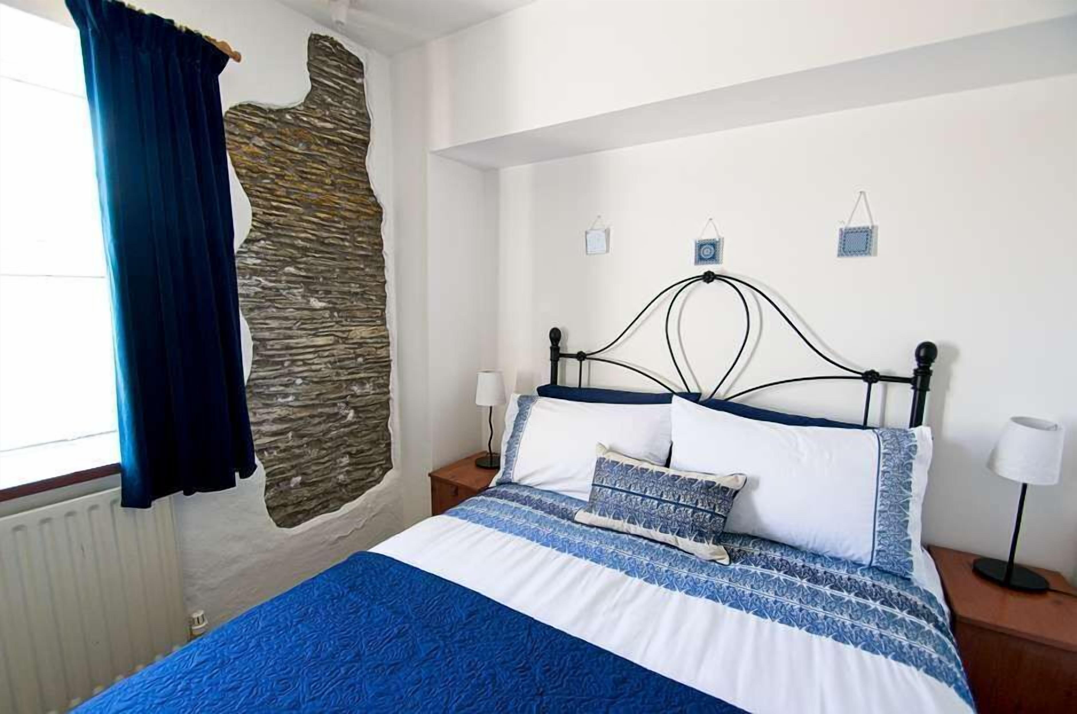A bedroom with a bed, a stone wall, a blue curtain, and bedside lamps.