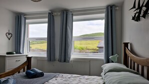 Ein Schlafzimmer mit Bett, Nachttisch, einem Fenster mit Vorhängen und Blick ins Freie.
