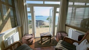 A room with a view of the sea, a wooden table, and two wicker chairs. - Gorgeous 2 bed apartment with large terrace overlooking Combesgate Beach (Woolacombe)