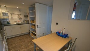 A compact kitchen with white cabinets, a tiled floor, and a dining table with chairs. - Gorgeous 2 bed apartment with large terrace overlooking Combesgate Beach (Woolacombe)
