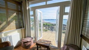 A room with a view of the sea, a wooden table, and a cushioned bench. - Gorgeous 2 bed apartment with large terrace overlooking Combesgate Beach (Woolacombe)