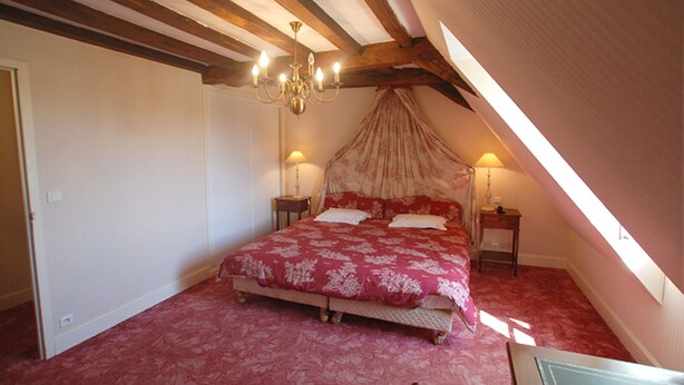 Une chambre à coucher avec un grand lit, deux tables de chevet, un lustre et une fenêtre donnant sur un beau paysage.