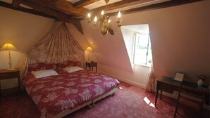 Une chambre à coucher avec un lit à baldaquin, deux lampes de chevet, un lustre et une petite table sur laquelle est posé un vase.