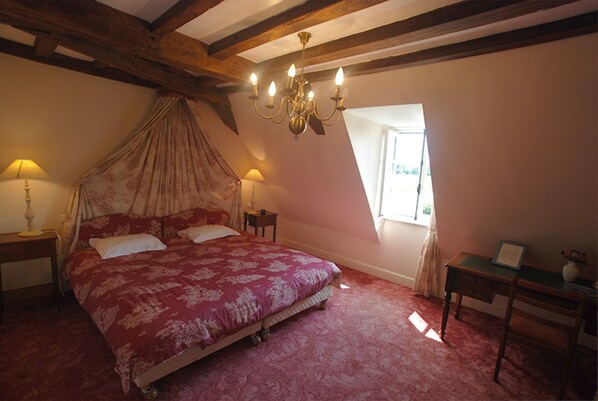 Un dormitorio con cama a dosel, dos lámparas de noche, un candelabro y una pequeña mesa con un florero.