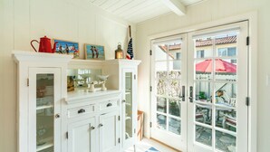 A white interior with a glass-fronted cabinet, a red teapot, and a framed picture. - Refined Coastal Escape a Block from West Beach! (Santa Barbara)
