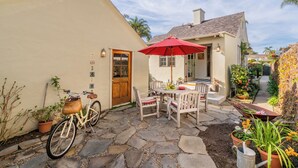A patio with stone flooring, a wooden table with chairs, a red umbrella, and a bicycle parked against a wall. - Refined Coastal Escape a Block from West Beach! (Santa Barbara)