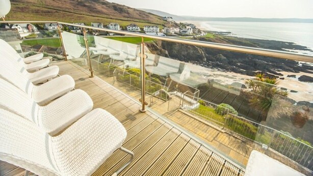 A deck with white wicker chairs overlooking a coastal landscape with houses and a beach. - Fabulous 3 bed apartment with amazing seaviews and balcony (Woolacombe)