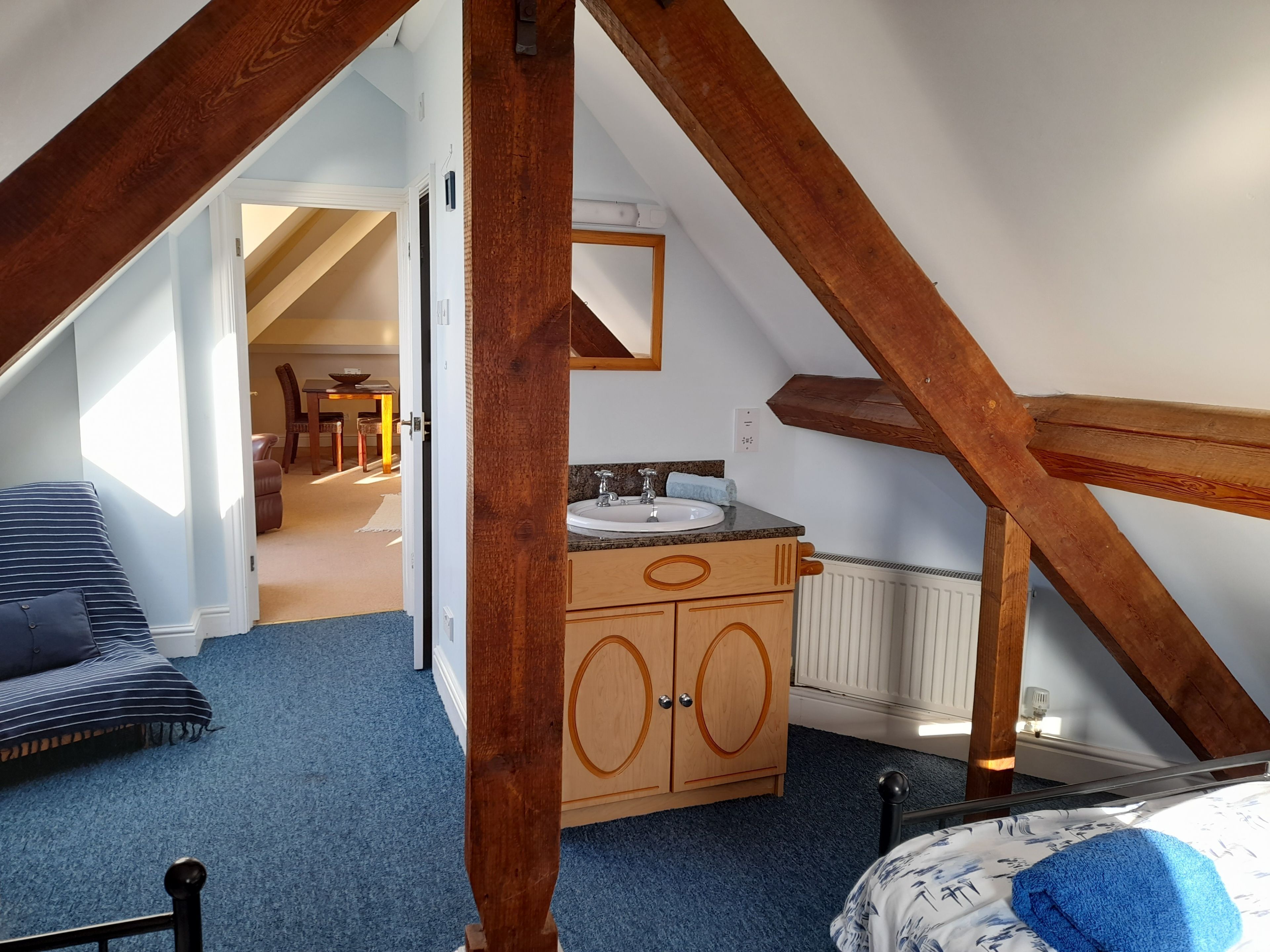 Une chambre avec un plafond en pente, des poutres en bois, un lit, une commode et une salle de bain avec un lavabo et un miroir.