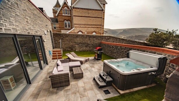 Eine Dachterrasse mit Whirlpool, Liegestühlen und einer Steinmauer.