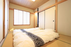 A traditional Japanese room with tatami flooring, a bed with a patterned bedspread, sliding doors, and a window with blinds. - TM house (Tokyo)