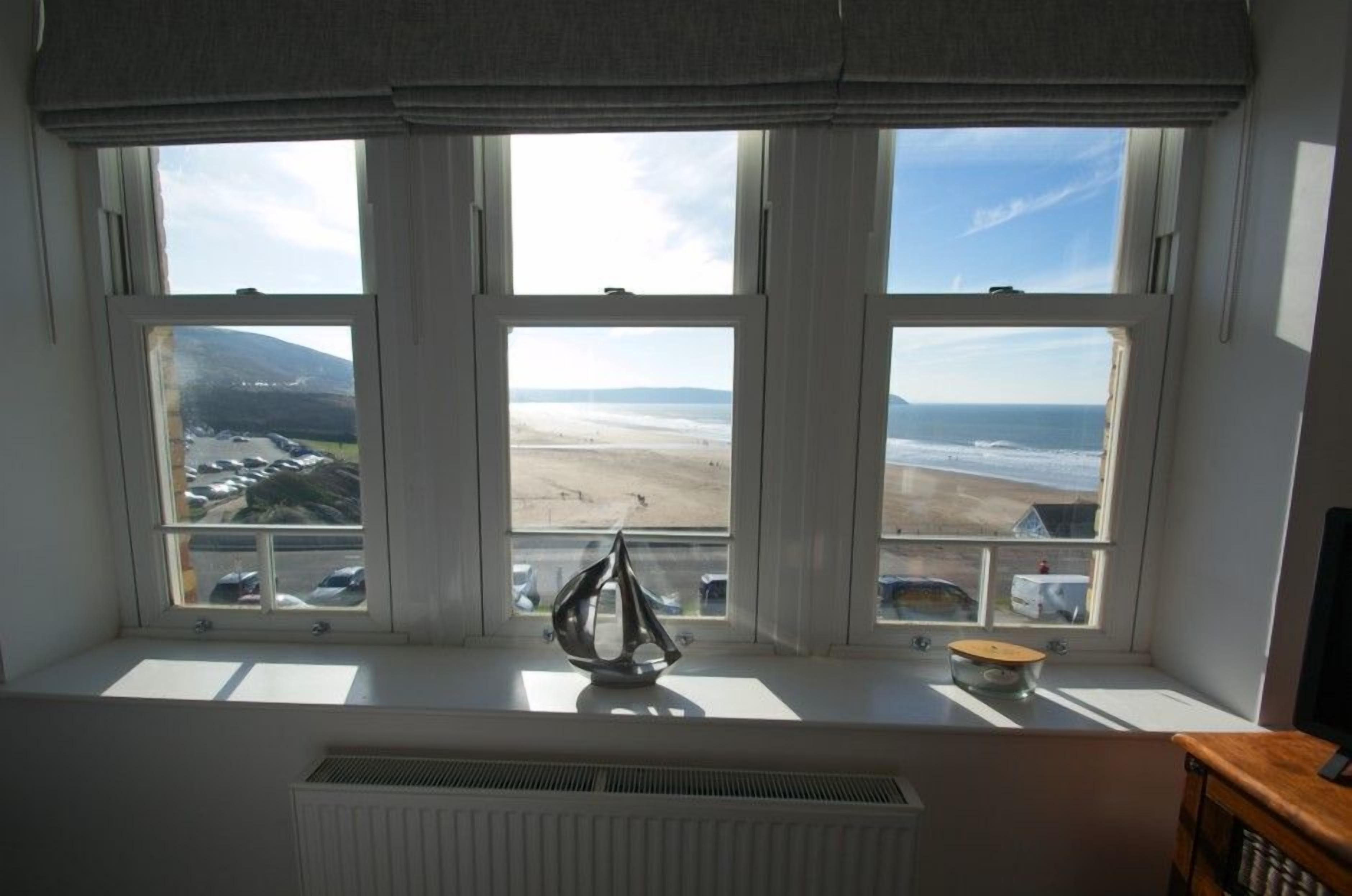 Een kamer met een groot raam dat uitkijkt op een strand en bergen.