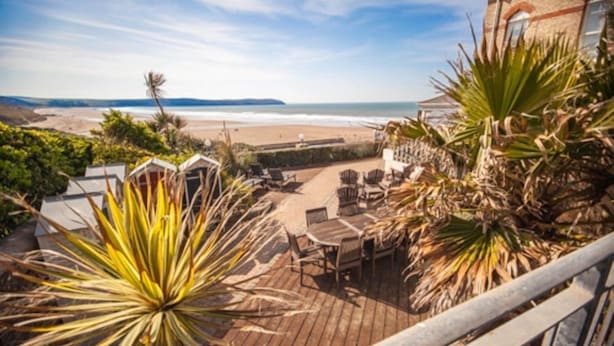 Eine Holzterrasse mit Gartenmöbeln mit Blick auf einen Strand.