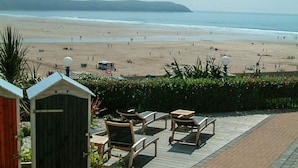 Blick auf einen Strand mit einer Holzterrasse, Stühlen und einem kleinen Schuppen.