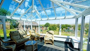 Ein Wintergarten mit Glasdach, Korbmöbeln und Blick ins Grüne.