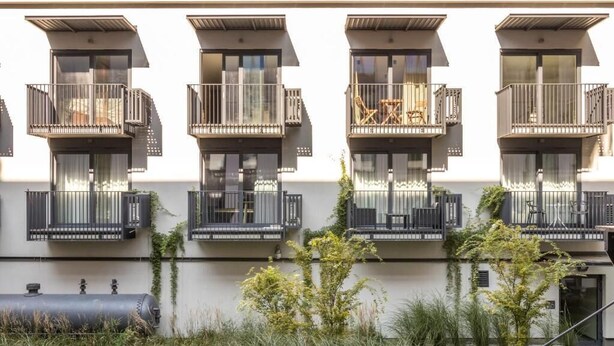 A modern building with multiple balconies, each with a small table and chair.