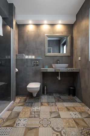 Et moderne badeværelse med et stort spejl, en skålhåndvask og et toilet.