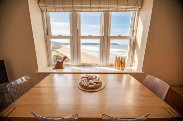 Une table à manger avec vue sur la plage, visible à travers une fenêtre.