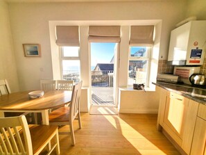 A bright kitchen with a dining area, large windows, and a view of the outside. - Smart 2 bed apartment opposite main beach with fab views and outside space (Woolacombe)