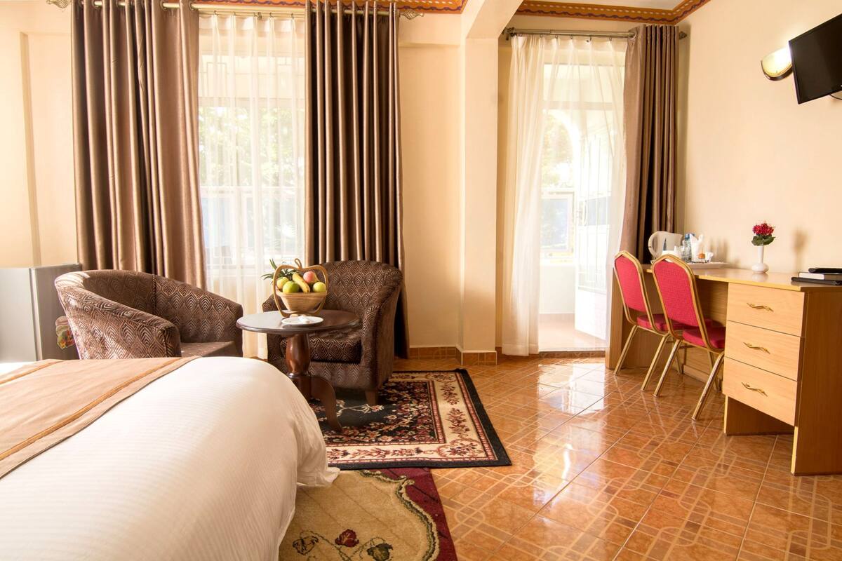 Habitación de hotel con cama, escritorio con silla, una mesita con frutero y televisor en la pared.