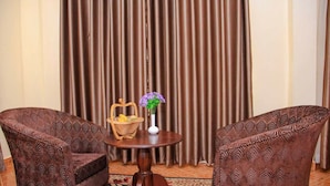 Una habitación con dos sillones estampados, una mesita redonda con una cesta y un florero, y un telón de fondo.