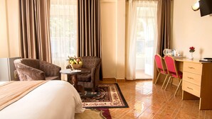 Habitación de hotel con cama, zona de estar con una silla y una mesita, escritorio con sillas y televisión montada en la pared.