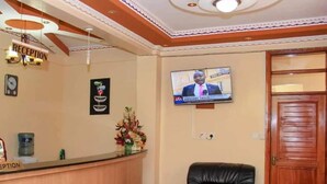 Una zona de recepción con un mostrador de madera, un letrero de recepción, un televisor montado en la pared y un sillón de cuero negro.