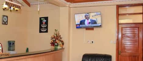 A reception area with a wooden counter, a reception sign, a television mounted on the wall, and a black leather chair.