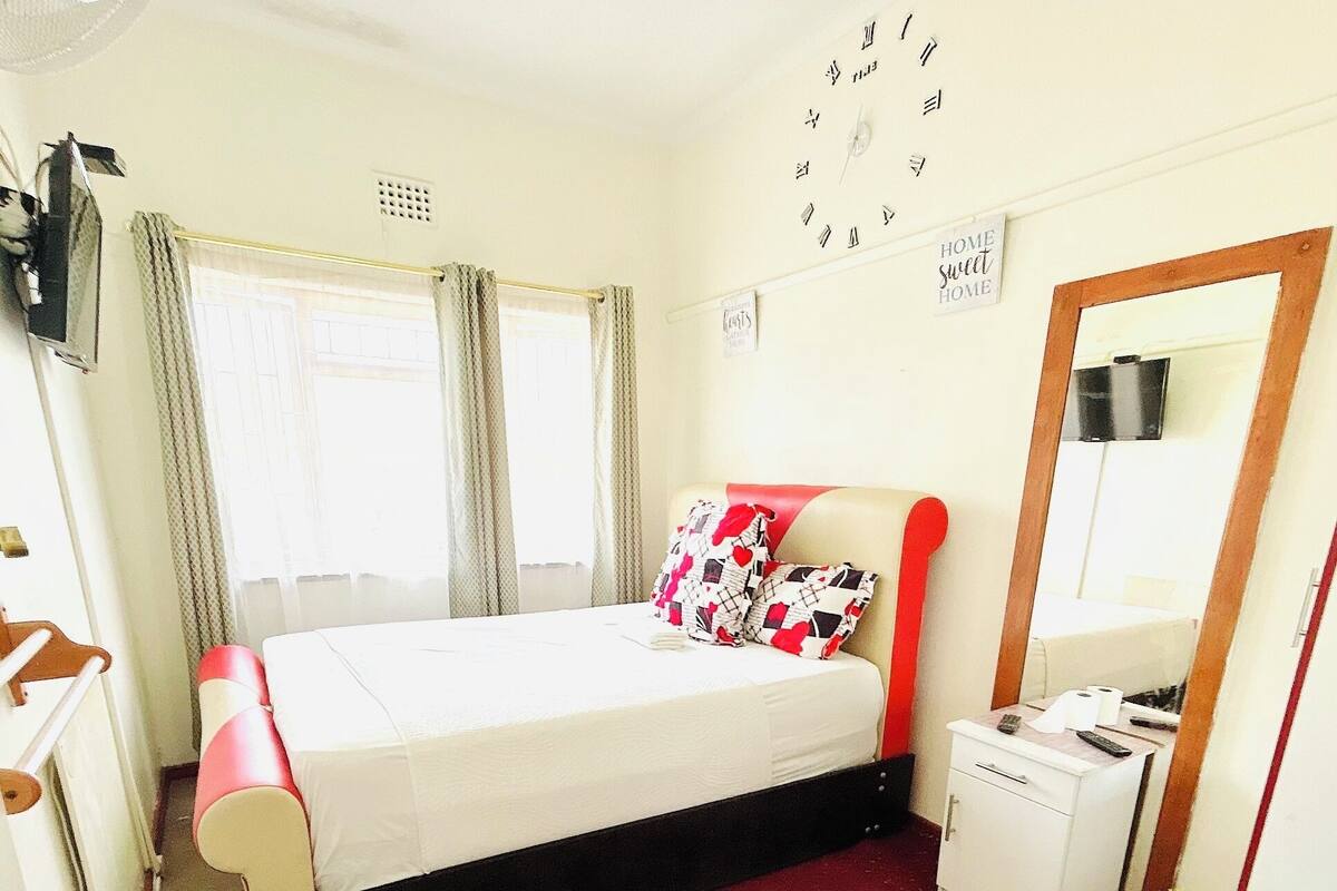 Una habitación de hotel con una cama, un pequeño escritorio, un espejo y una alfombra roja.