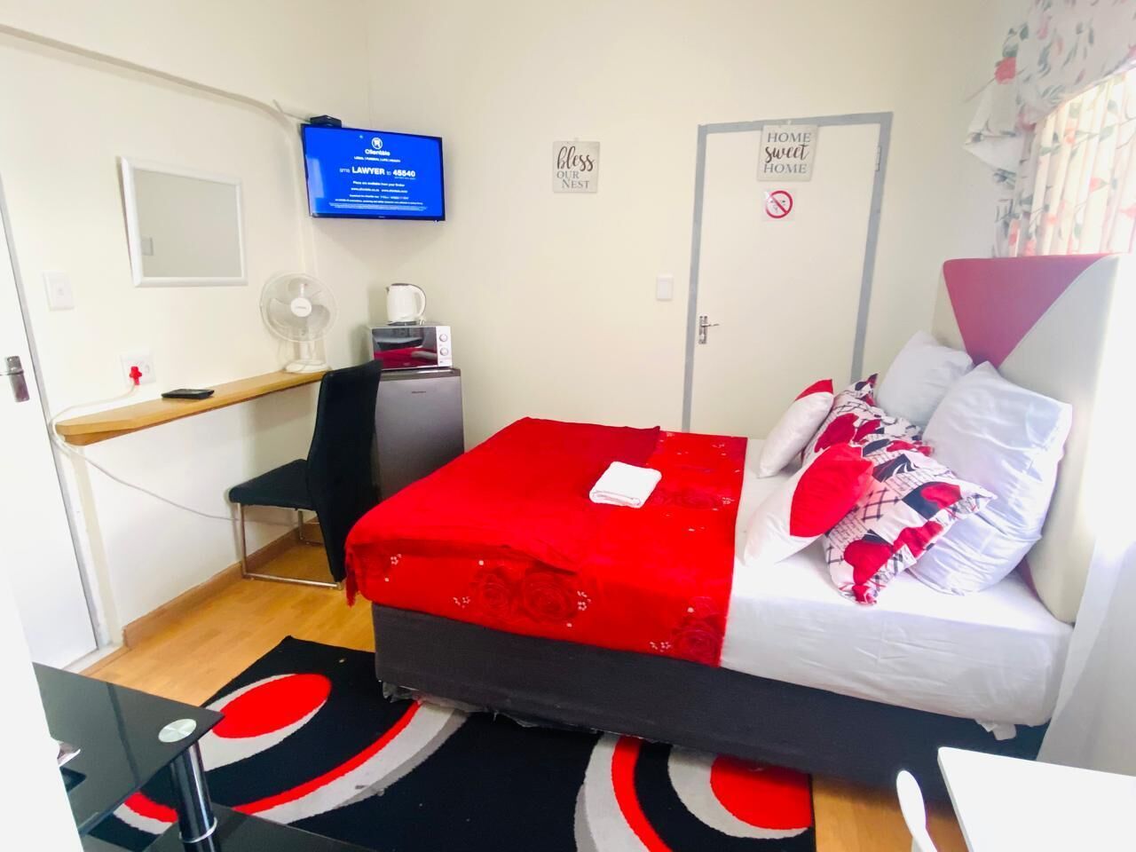 Une petite pièce comprenant un lit, un bureau, une chaise, un téléviseur et une porte avec une pancarte.