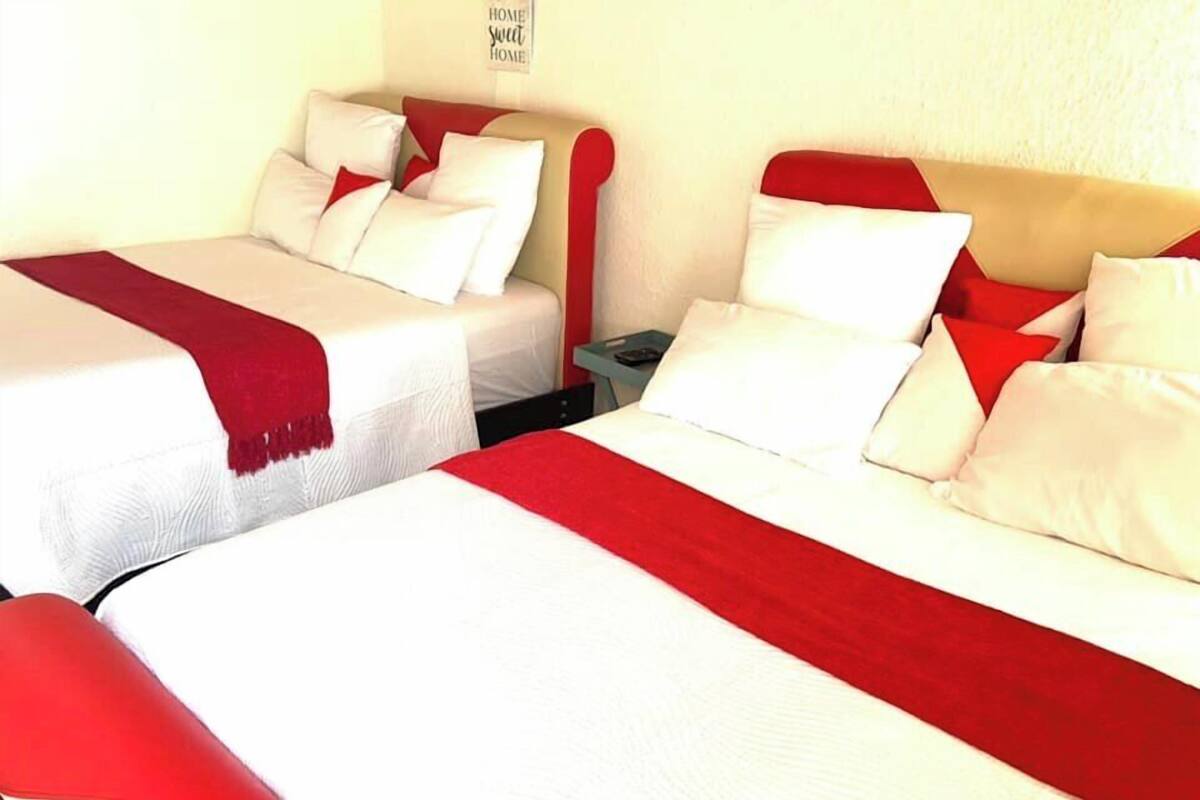 Habitación de hotel con dos camas, cada una con ropa blanca y detalles rojos.