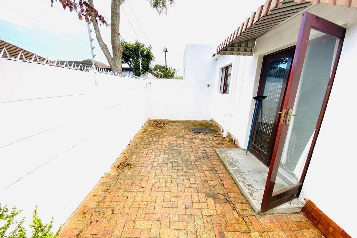 Un patio empedrado con una pared blanca y una puerta que da a un acceso cubierto.
