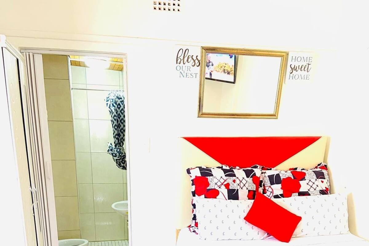 Un dormitorio con cama, un baño con inodoro y lavamanos, y una puerta corrediza de vidrio que da al baño.