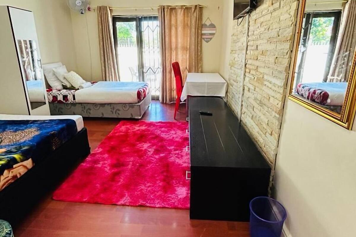Una habitación pequeña con cama, escritorio, espejo y una alfombra roja.
