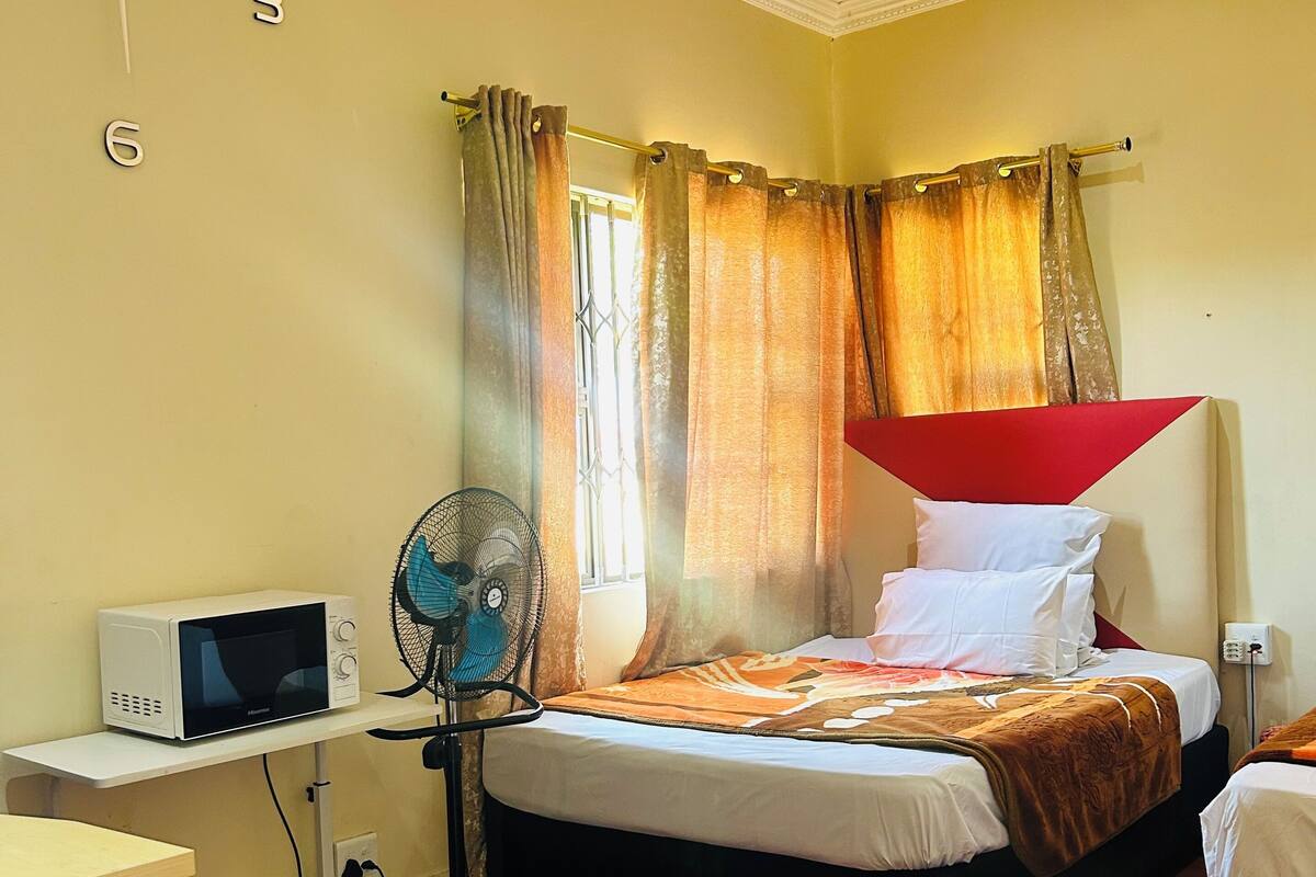 Un dormitorio con cama, microondas, ventilador y escritorio.