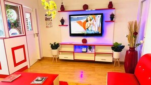 Ein modernes Wohnzimmer mit einem an der Wand befestigten Flachbildfernseher, einem roten Sofa, einem roten Hocker und einem kleinen Couchtisch.