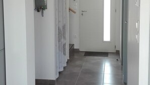 Un pasillo con suelo de baldosas, una puerta blanca al final y una ventana con luz natural.