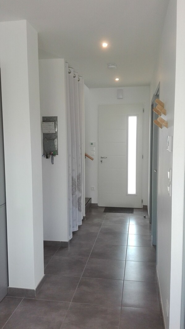 A hallway with a tiled floor, a white door at the end, and a window with natural light.