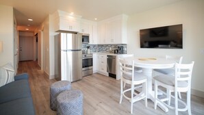 A compact kitchen with white cabinets, a stainless steel refrigerator, and a dining area with white chairs and a round table.