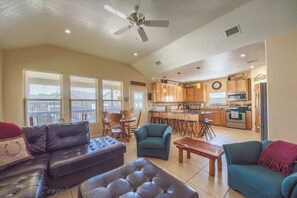 A spacious living area with a sofa, armchair, and ottoman, a kitchen with wooden cabinets and appliances, and a dining area with chairs.