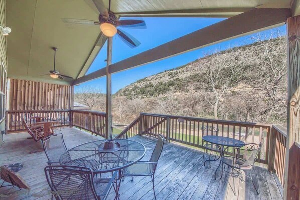 A covered outdoor deck with a table and chairs, a ceiling fan, and a view of a hilly landscape.