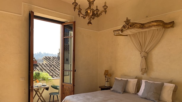 A bedroom with a large bed, a chandelier, a nightstand with a lamp, and a view of the outside through an open door. - DUOMO, MEDIEVAL TOWER Florence: SANTA CROCE in the DONATI TOWER 4th floor w/lift (Firenze)