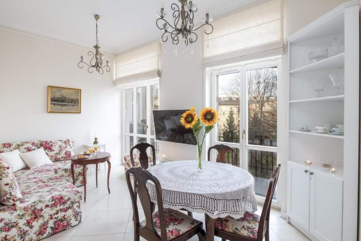 A dining area with a round table, floral sofa, and a chandelier.