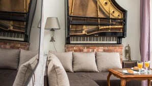 A room with a grand piano, a sofa, and a table with breakfast items. - Apartments Wygoda A4You (Kraków)