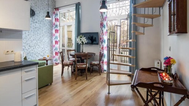 A modern kitchen with a brick wall, wooden flooring, and a dining area with a table and chairs. - Apartments Wygoda A4You (Kraków)