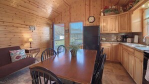 A wooden interior with a dining table, chairs, a sofa, a refrigerator, and wooden cabinets. - RR 9122WC Wine Cup Cabin (New Braunfels)