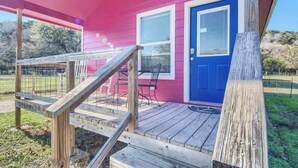 A pink house with a blue door, a wooden deck, and a covered porch. - RR 9122WC Wine Cup Cabin (New Braunfels)