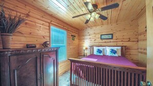 A wooden cabin room with a bed, a ceiling fan, a dresser, and a window with blinds. - RR 9122WC Wine Cup Cabin (New Braunfels)