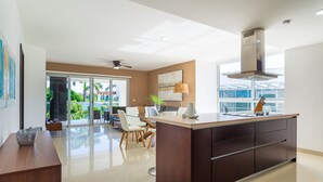 A modern kitchen with a central island, a ceiling fan, and a large window providing a view of the outdoors. - Garden View  Apartment Beach Accesible 2 bedroom 2 bath   Casa Sol (Playa del Carmen)