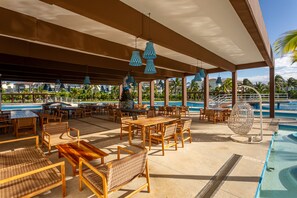 An outdoor seating area with wooden tables and wicker chairs, overlooking a pool and palm trees. - Garden View  Apartment Beach Accesible 2 bedroom 2 bath   Casa Sol (Playa del Carmen)