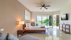 A modern bedroom with a bed, bedside table, lamp, and a TV on a wooden stand. - Garden View  Apartment Beach Accesible 2 bedroom 2 bath   Casa Sol (Playa del Carmen)